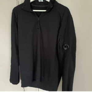 Svart half zip tröja från C.P. Company - Säljer min svarta half zip från CP company. Tröjan är i utmärkt skick och äkta med prislapp som följer med och QR kod. Priset är inte hugget i sten kom gärna med förslag!