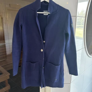 Marinblå cardigan jacka från Sebago - Snygg marinblå cardigan jacka från Sebago med två stora fickor framtill och silverfärgade knappar. Tröj kavajen  är stickad, har lång ärm och en stilren krage. Perfekt för dig som gillar klassisk och avslappnad stil. Hör av er för frågor eller funderingar!🙌🏻