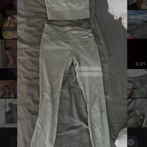 Tränings set från stronger  - Säljer en grå linnetopp från Stronger med sportig look. Toppen har breda axelband, rund halsringning och coola silvriga prickdetaljer vid axlarna. Materialet är stretchigt och skönt, perfekt för träning eller gym. Matcha med tights för en komplett träningsoutfit!