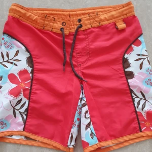Badshorts - Snygga badshorts från Body Zone i rött och orange med blommigt mönster i vitt, rosa, blått och brunt. Shortsen har snörning i midjan och coola kontrastpaneler på sidorna. Perfekta för stranden eller poolen!