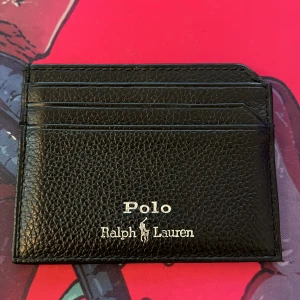 Svart korthållare Polo Ralph Lauren - Slimmad svart korthållare från Polo Ralph Lauren i skinn. Snygg och stilren med flera kortfack på båda sidor och silverfärgad logga. Pris går att diskuteras!