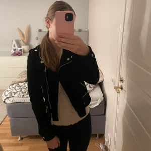 Svart mockajacka från Vero Moda - Snygg svart mockajacka från Vero Moda med silvriga dragkedjor och detaljer. Jackan har klassisk bikerstil, lång ärm och flera fickor med dragkedja. Perfekt för dig som vill ha en stilren och edgy look.