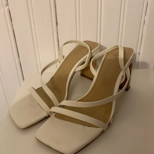 Vita sandaler med klack från H&M - Stilrena vita sandaler från H&M med fyrkantig tå och smala remmar. Skorna har en hög blockklack och öppen tå, vilket ger en trendig look. Ca 7 cm. Använda st 36 