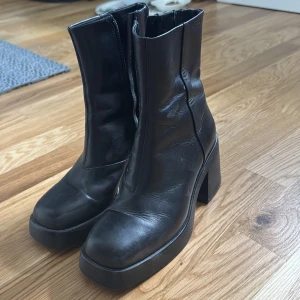 Svarta boots med klack och dragkedja - Snygga svarta boots från Vagabond i skinn med chunky klack och platt sula. Modellen har rund tå och dragkedja på insidan för enkel påtagning. Perfekta för dig som vill ha en stilren och edgy look till höst och vinter. Använda endast ett fåtal gånger. Storlek 37. Nypris ≈ 1500kr.