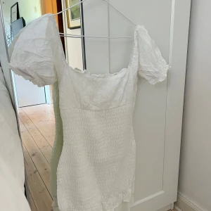 Vit kort sommarklänning  - Superfin vit kort klänning med puffärmar och smockad midja. Stretchig så passar xs-m