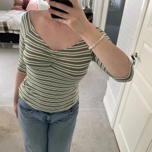 Randig v-ringad topp  - Säljer en slim, randig topp med v-ringning och trekvartsärm från Cubus. Färgerna är grönt, svart och vitt. Sitter tight och har en snygg, figurnära passform. Storlek M.    Använt fåtal gånger