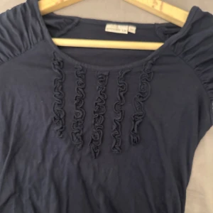 Mörkblå topp med rysch från Stockh LM - Supersöt mörkblå topp från Stockh LM i mjuk bomull. Den har korta puffärmar och snygga ryschdetaljer framtill som ger en cool touch. Perfekt för dig som gillar en enkel men ändå unik stil. Älskar denna toppen men är för liten för mig. Aldrig använd jättefint skick. 