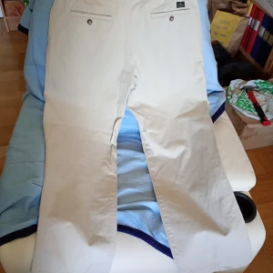 Beiga chinos i bomull, raka ben stl 36/32 - Snygga beiga chinos med raka ben och klassisk passform. Byxorna är tillverkade i 100% bomull och har två bakfickor med knapp samt sidofickor. Perfekta för en clean och stilren look.stl 36/32.