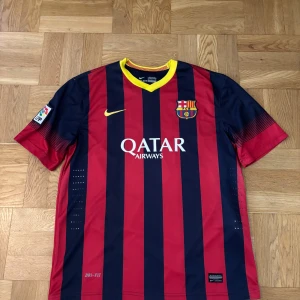 FC Barcelona tröja med xavi - Barças klassiska randiga matchtröja med Xavi och nummer 6 på ryggen. Röd och mörkblå med gula detaljer. kortärmad och med officiella La Liga-märket på ärmen.