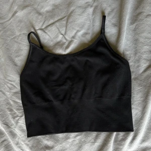 Svart linnetopp från H&M Sport - En svart, enkel linnetopp från H&M Sport med smala justerbara axelband och ribbad nederkant. Toppen är croppad och har en stilren, sportig look som passar perfekt till träning eller chill. Materialet är mjukt och stretchigt för extra komfort.