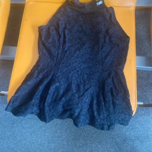 Fin svart sommar top  - Supersnygg svart  sommar top  med spetsdetaljer och hög hals. Topen är ärmlös och har en figurnära passform upptill med utsvängd kjol. Perfekt för dig som vill sticka ut med en elegant look.