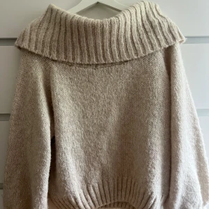 Beige stickad tröja från Gina Tricot - Supermysig beige stickad tröja från Gina Tricot med off-shoulder krage i nyskick. Tröjan har lång ärm och en loose fit som ger en chill vibe. Perfekt för r höst och vinter samt kyliga sommarkvällar. Materialet är mjukt och värmande, perfekt för kalla dagar.