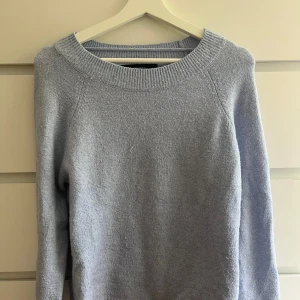 Ljusblå stickad tröja Vero Moda - Mysig ljusblå stickad tröja från Vero Moda med rund halsringning och långa ärmar. Tröjan har en ribbad kant vid halsen och är perfekt för kyliga dagar. 