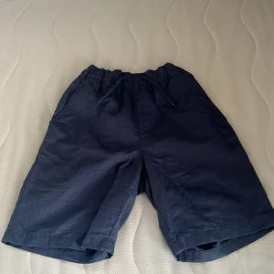 Mörkblå shorts med snörning - Snygga mörkblå shorts med elastisk midja och dragsko för skön passform. De har raka ben och sidfickor, perfekta för varma dagar. Materialet känns lätt och luftigt, troligen bomull eller linne. Enkla att matcha med t-shirt eller hoodie. 