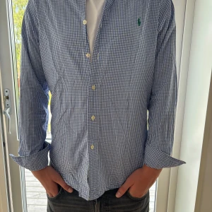 Blårutig skjorta Ralph Lauren Slim Fit - Snygg blårutig skjorta från Ralph Lauren i slim fit-modell. Skjortan har klassisk krage, långa ärmar och knäppning framtill. Broderad grön logga på bröstet. Tillverkad i mjuk bomull som känns skön mot huden.