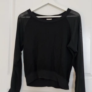 Svart långärmad tröja från H&M - Svart långärmad tröja från H&M i storlek 34. Tröjan har transparenta meshärmar och axelparti som ger en snygg kontrast till den helsvarta kroppen. Perfekt för dig som gillar en stilren look med lite edge.