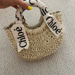 Väska i rotting - Superfin handväska i flätad beige strå med rundade former. Väskan har ett prickigt innerfoder i ljusgrått och vitt. Perfekt accessoar för en trendig look. Rem tillkommer i samma material