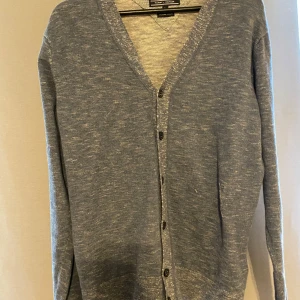 Blåmelerad kofta från Tommy Hilfiger - Snygg blåmelerad kofta från Tommy Hilfiger med v-ringning och knappar framtill. Långärmad och i mjuk bomullsblandning, perfekt att slänga på sig över en t-shirt. Enkel och stilren design som funkar till det mesta.