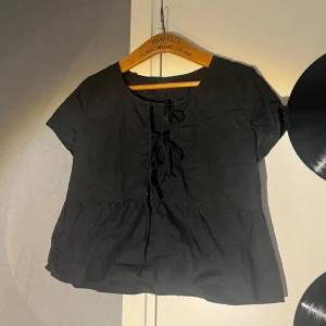 Svart blus med snörning Gina Tricot - Supersöt svart blus från Gina Tricot med korta ärmar och snörningsdetalj framtill. Modellen är lite lösare med volang nedtill och rund halsringning. Perfekt att styla med jeans eller kjol för en chill look.