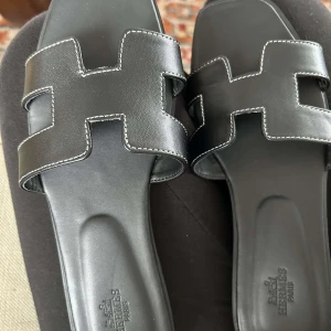 Svarta Oran sandaler storlek 38 - Svarta Oran sandaler med vita sömmar, storlek 38. Platt sula, öppen tå, bekväma.