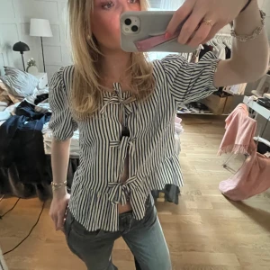 Randig blus med knyt fram - Säljer en blåvit randig blus med kort ärm och knyt fram både vid byst och midja. Blusen har volangkant nertill och är tillverkad i ett lätt bomullstyg. Perfekt för vår och sommar! Storlek 38 men är mer som en 36 eller 34