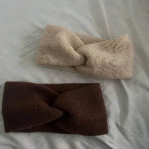 Stickade twistade pannband i beige och brunt - Två stickade pannband i mjuk kvalitet, ett i beige och ett i brunt. Båda har en twistad knut framtill som detalj. Perfekta för att hålla öronen varma under kyliga dagar