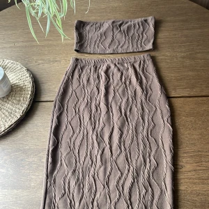 Brun ribbad kjol från SHEIN - Brun, figurnära kjol och topp från SHEIN med ribbat, vågigt mönster. Kjolen är midilång och har en mjuk, stretchig känsla. Perfekt att matcha med den medföljande tubtoppen för en snygg look.
