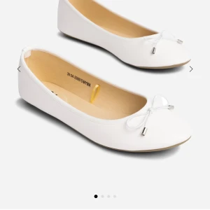 Vita ballerinaskor med rosett - Snygga vita ballerinaskor med en söt rosett framtill. Skorna har rund tå och platt sula, vilket gör dem bekväma och stilrena. Perfekta att matcha med både jeans och klänning för en fräsch look. Helt nya aldrig använda! Prislapp sitter på! 