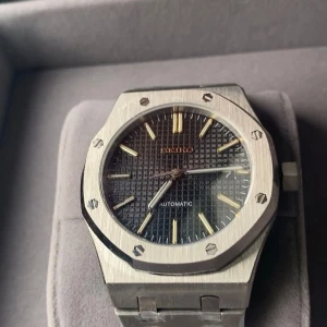 Seiko AP - Säljer en Seiko herrklocka med automatisk urverk. Klockan har en åttakantig boett i borstat silverfärgat stål och svart urtavla med guldiga index och visare. Länken är också i silverfärgat stål och klockan har en sportig men stilren design.