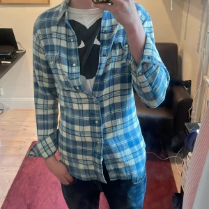 Blå och vit rutig skjorta från Polo Ralph Lauren - Säljer en klassisk blå och vit rutig skjorta från Polo Ralph Lauren i storlek XS. Skjortan har långa ärmar, knappar framtill och två snygga bröstfickor. På vissa ställen har färgen blekts lite som syns på bild tre. Annars är skjortan i perfekt skick! Priset är ej hugget i stenen.