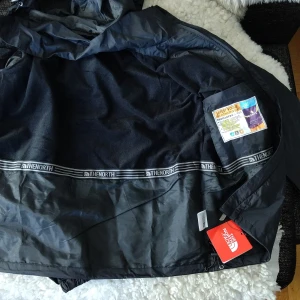 Svart vindjacka från The North Face Summit Series - Säljer en svart vindjacka från The North Face Summit Series. Jackan har huva, dragkedja och är tillverkad i ett lätt syntetmaterial som är både vattentätt och andas. Perfekt för utomhusaktiviteter och sport.