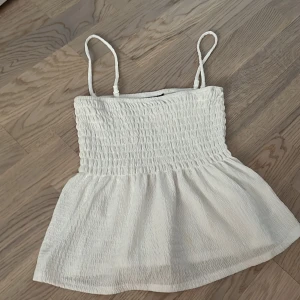 Vit smockad linnetopp från Gina Tricot - Säljer en söt vit linnetopp från Gina Tricot med smockad överdel och tunna axelband. Toppen har en lätt utställd nederdel och är perfekt för varma dagar. Man kan även ta av axelbanden för att gör en pdf shoulder topp! 