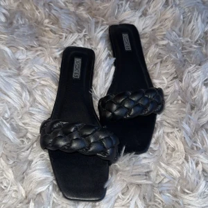 Svarta flätade sandaler med fyrkantig tå - Säljer ett par svarta sandaler med bred, flätad rem över foten och fyrkantig tå. Helt oanvända. 