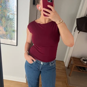 Vinröd topp från Nelly - Säljer en vinröd topp från Nelly med kort ärm och rund halsringning. Toppen har en tight passform och är tillverkad i ett mjukt, stretchigt material. Perfekt att styla med jeans eller kjol.