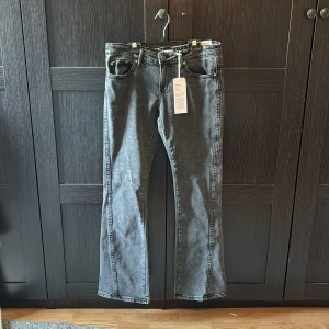 Grå lowrise twisted-bootcut jeans från Gina Tricot - Väldigt fina low rise twisted-bootcut jeans från Gina Tricot med fin design på fickorna, har aldrig använts och är i väldigt bra skick!