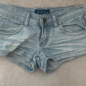 Ljusblå jeansshorts från M.O Jeans - Säljer ett par ljusblå jeansshorts med klassisk femficksdesign och knappgylf. Shortsen har låg midja och är i en kort modell med slitna detaljer för en avslappnad look.