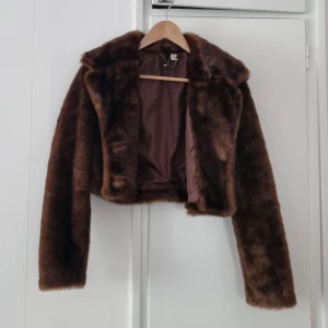 Brun pälsjacka med krage - Säljer en brun pälsjacka med krage och knappar framtill. Jackan är croppad och har långa ärmar. Perfekt för dig som vill ha en trendig och mysig look.
