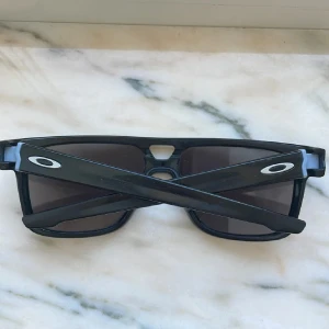 Oakley Crossrange Patch Matte Black Solglasögon - Snygga solglasögon från Oakley i modellen Crossrange Patch. De har en matt svart båge och mörka rektangulära linser. Perfekta för dig som vill ha en sportig och stilren look. Passar både till vardags och aktivitet.
