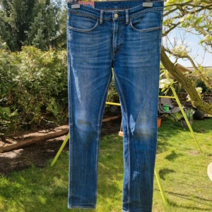 Blå jeans från Acne Studios Blå Konst - Säljer ett par klassiska blå jeans från Acne Studios Blå Konst. Jeansen har fem fickor, raka ben och normal passform. Snygga detaljer med orange sömmar och knappgylf. Perfekta till vardags för en stilren look. 38cm i midjan, 108cm längd 