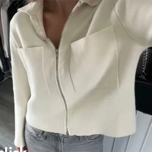 Vit kofta med dragkedja - Snygg vit kofta med dragkedja framtill och två stora fickor på bröstet. Jackan har krage och långa ärmar, perfekt för en stilren och modern look. Passar till jeans eller kjol för en trendig outfit. Använd 2 gånger