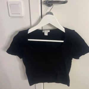 Svart croppad topp från Amisu - Säljer en svart croppad topp från Amisu med korta ärmar och rundad urringning. Perfekt att matcha med höga jeans eller kjol. Enkel och stilren design som passar till många olika outfits.