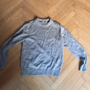 Ljusgrå stickad tröja - En stilren ljusgrå stickad tröja med rund halsringning och ribbade muddar vid ärmslut och nederkant.  Helt oanvänd