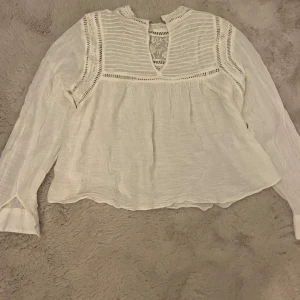 En tunn sommar topp/skjorta i vitt - En somrig topp/skjorta perfekt för stranden eller finare location. Plagget har knappar längst ner på armarna och finare broderingar i tyget.