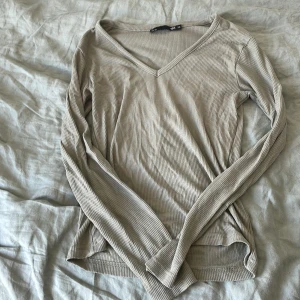 Grön ribbad långärmad tröja med v-ringning - Säljer en grön ribbad långärmad tröja i storlek XS. Tröjan har v-ringad hals och är i ett mjukt, stretchigt material som sitter snyggt på kroppen. Perfekt basplagg till garderoben!