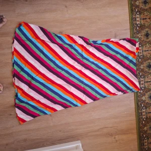 Färgglad långkjol med diagonala ränder - Säljer en långkjol med färgglada diagonala ränder i rosa, röd, blå, lila och orange. Kjolen har en rak passform och är tillverkad i ett lätt och mjukt material, perfekt för varma dagar.