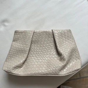 Beige kuvertväska med ormmönster - Säljer en beige kuvertväska i syntetmaterial med stilrent ormmönster. Väskan har magnetlås i guld och är perfekt för att bära det viktigaste. Enkel och trendig design som passar till många tillfällen. Aldrig använd och mycket bra material 