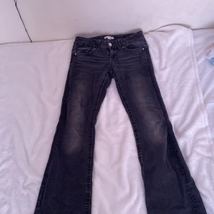 Svarta bootcut jeans - Säljer ett par svarta bootcut jeans med lätt slitning och klassisk femficksdesign. Jeansen har knapp och dragkedja framtill samt raka bakfickor med knappdetalj. Perfekta för dig som gillar en tidlös och avslappnad stil.