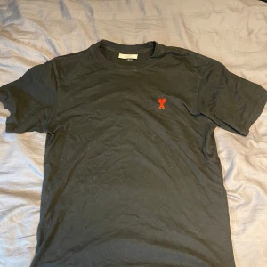 Svart t-shirt från Ami Alexandre Mattiussi - Svart t-shirt från Ami med röd broderad logga i form av ett hjärta på bröstet. Klassisk passform som är insyd själv och rund halsringning. Perfekt för en stilren och enkel look. Den är L men insydd för att bli figursydd! Byten är intressant!