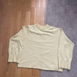 Ljusgul stickad tröja med rund hals - Mysig ljusgul stickad tröja med rund hals och långa ärmar. Tröjan har breda ribbade muddar vid ärmslut och nederkant, samt en avslappnad passform. Perfekt för lager-på-lager under kyliga dagar.