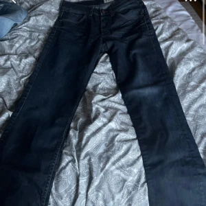 Mörkblå raka jeansbyxor - Säljer ett par svarta jeansbyxor med klassisk femficksdesign och raka ben. Byxorna har normal passform och är perfekta för en stilren look. Inga synliga detaljer som slits eller broderier, bara en enkel och tidlös design.